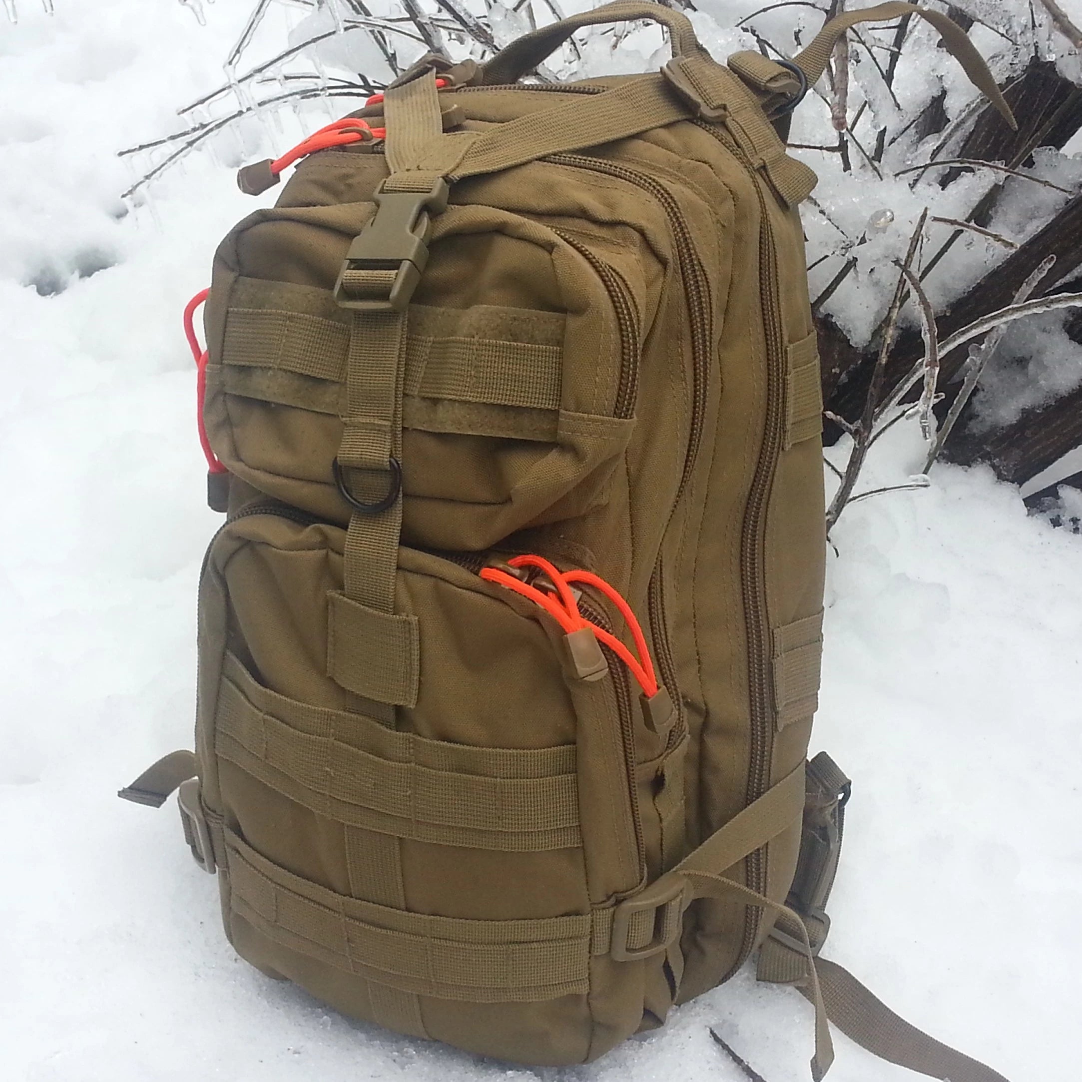 Brown tactical backpack with orange straps on a snowy background