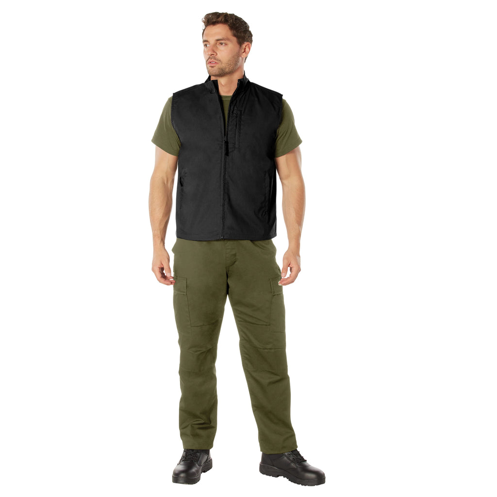 Man wearing a black vest over a green shirt with matching pants on a white background
