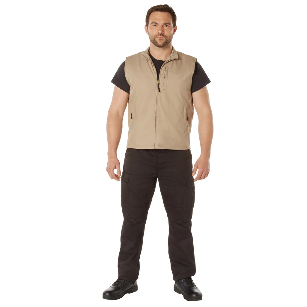 Man wearing a beige vest over a black shirt with black pants on a white background